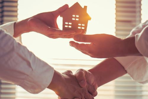 Close up of shaking hands while handing over a small wooden house