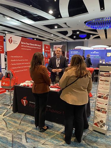 two attendees talking with a representative at the American Heart Association PAN booth at the Highlights of Heckerling conference