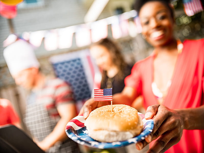 focus on a sandwich on a paper plate being held by a smiling woman at an outdoor celebration
