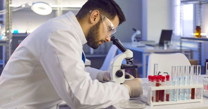 stock photo of male researcher looking through microscope