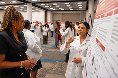 An American Heart Association Undergraduate Scholar is presenting her poster to a Symposium attendee.