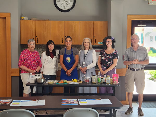 a group of Rural at Heart volunteers posing together in a kitchen with ingredients laid out for a recipe
